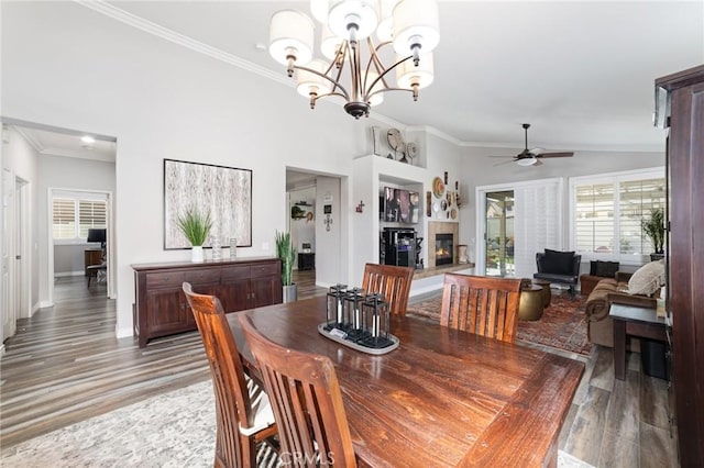 dining space featuring high vaulted ceiling, ceiling fan with notable chandelier, light wood finished floors, a glass covered fireplace, and crown molding