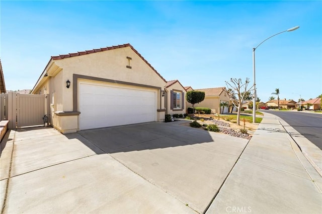 mediterranean / spanish-style house with a garage, concrete driveway, a tiled roof, a gate, and stucco siding