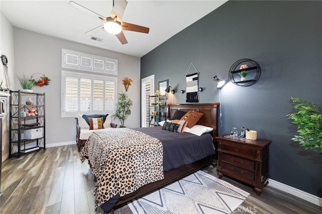 bedroom featuring a ceiling fan, visible vents, baseboards, and wood finished floors