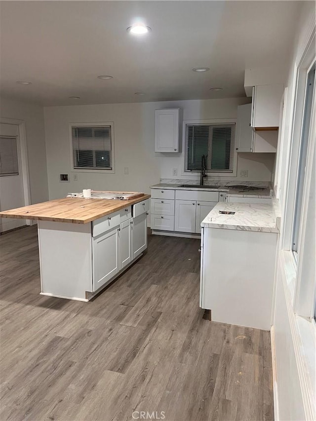 kitchen with white cabinets, butcher block counters, a kitchen island, wood finished floors, and a sink