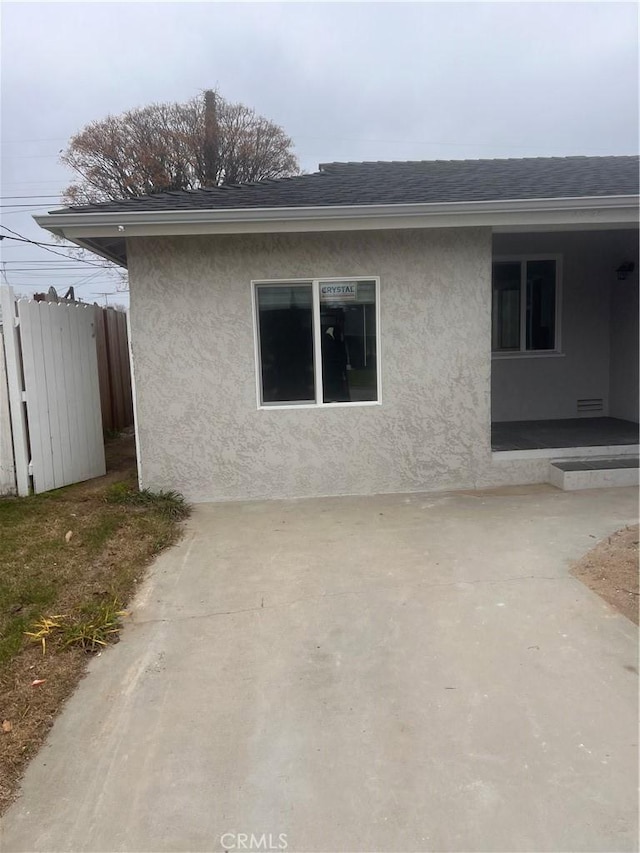 view of property exterior featuring a shingled roof, a patio area, fence, and stucco siding