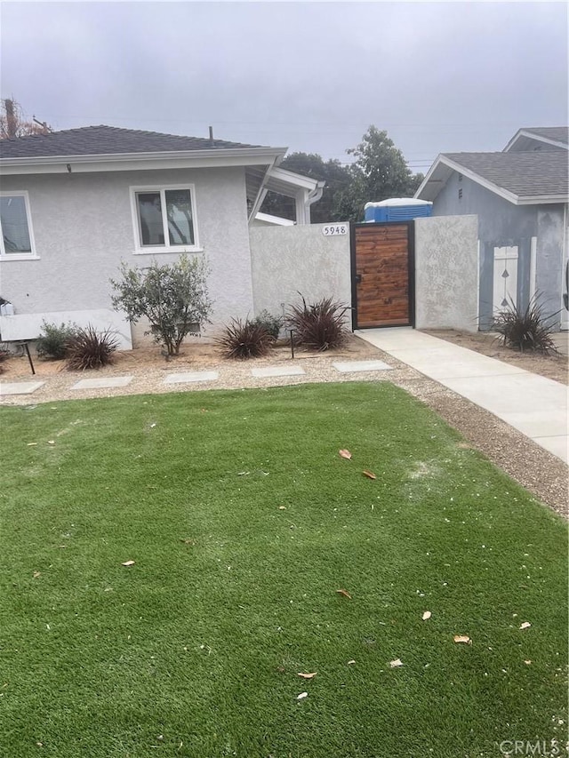 view of side of property featuring a lawn, a gate, and stucco siding