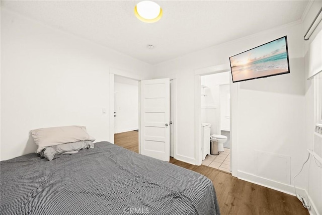 bedroom featuring connected bathroom, baseboards, and wood finished floors