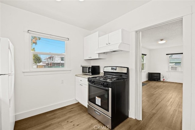 kitchen featuring light wood finished floors, white cabinets, appliances with stainless steel finishes, under cabinet range hood, and a wealth of natural light