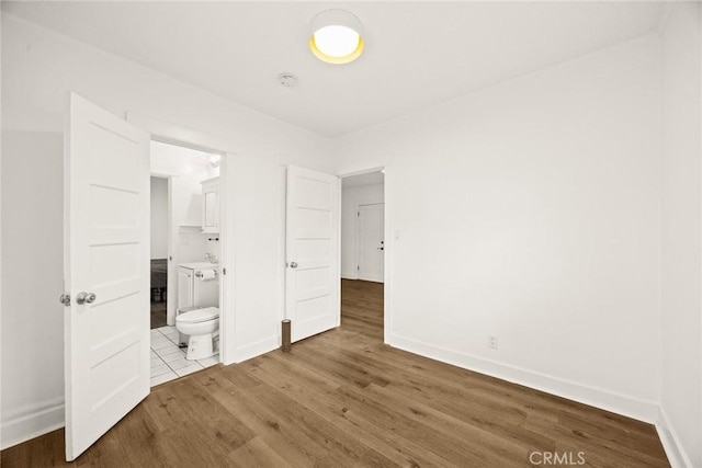 unfurnished bedroom featuring connected bathroom, baseboards, and wood finished floors