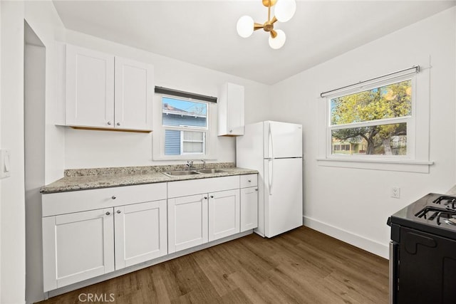 kitchen with a sink, white cabinetry, freestanding refrigerator, dark wood-style floors, and gas stove