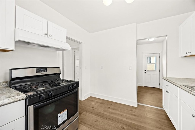 kitchen with light wood finished floors, white cabinetry, stainless steel gas range oven, under cabinet range hood, and baseboards