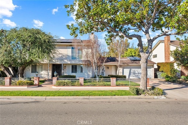 traditional-style home featuring a fenced front yard, driveway, an attached garage, and solar panels