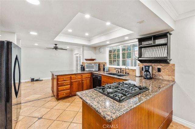 kitchen with black appliances, a tray ceiling, a peninsula, and a sink