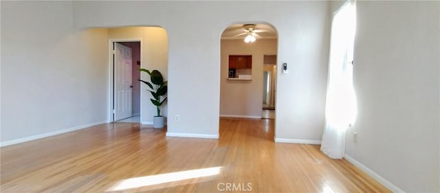 empty room featuring arched walkways, light wood-type flooring, and baseboards