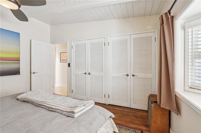 bedroom featuring vaulted ceiling with beams, wooden ceiling, wood finished floors, a ceiling fan, and multiple closets