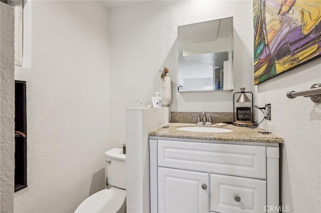 half bath with toilet, a textured wall, and vanity