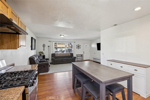 kitchen with light wood finished floors, open floor plan, a textured ceiling, under cabinet range hood, and stainless steel range with gas stovetop