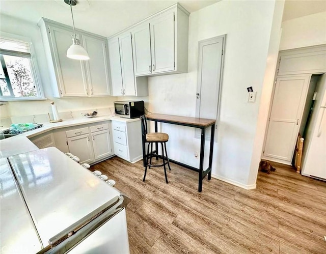 kitchen featuring light wood-style flooring, decorative light fixtures, stainless steel microwave, light countertops, and baseboards