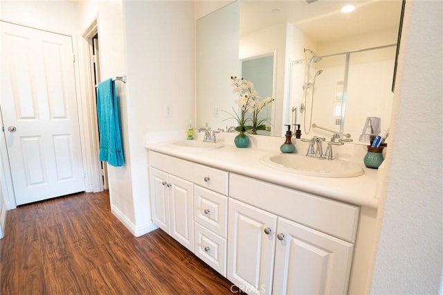 full bathroom with a shower, double vanity, a sink, and wood finished floors