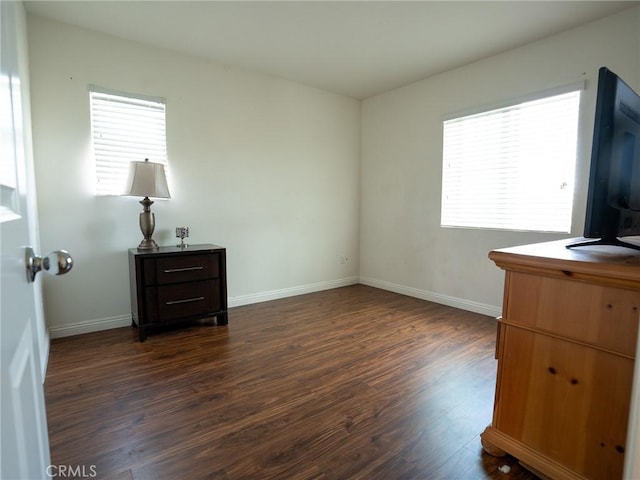 unfurnished bedroom featuring multiple windows, baseboards, and dark wood-type flooring