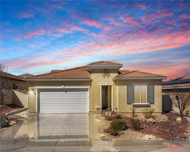 mediterranean / spanish house featuring an attached garage, fence, a tile roof, driveway, and stucco siding