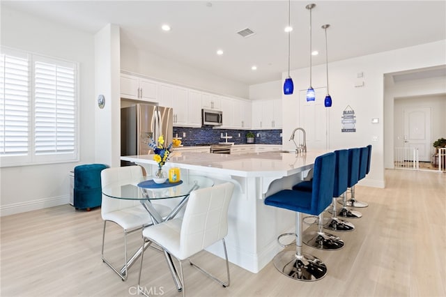 kitchen featuring a kitchen breakfast bar, light countertops, stainless steel appliances, white cabinetry, and backsplash