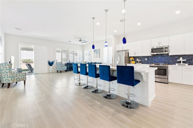 kitchen with a breakfast bar, a center island with sink, stainless steel appliances, tasteful backsplash, and light countertops