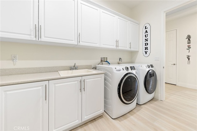 washroom with cabinet space, baseboards, washer and dryer, light wood-style floors, and a sink