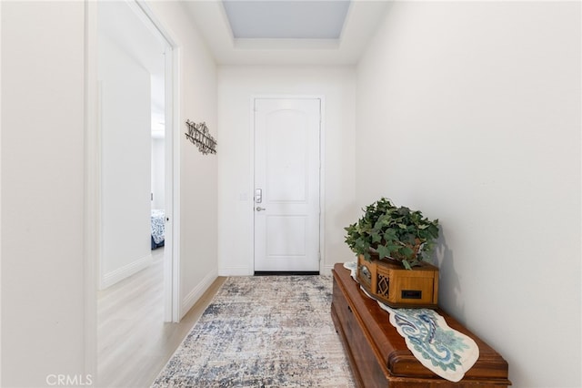 doorway to outside with light wood-style floors, baseboards, and a raised ceiling