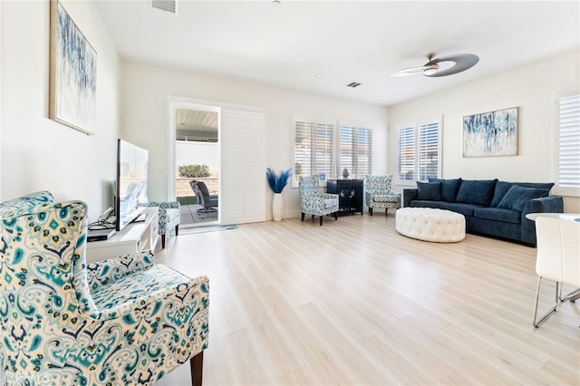 living area featuring a healthy amount of sunlight, a ceiling fan, visible vents, and wood finished floors