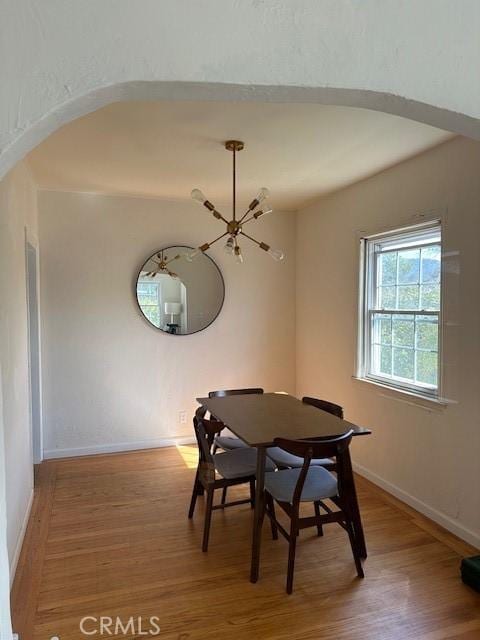 dining area featuring arched walkways, baseboards, and wood finished floors