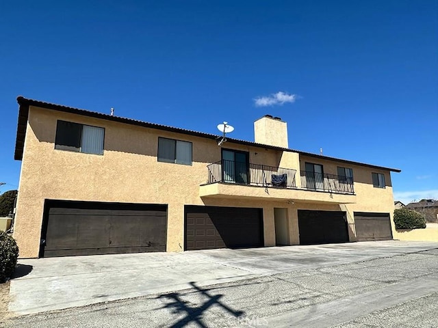 multi unit property featuring a balcony, an attached garage, a chimney, and stucco siding