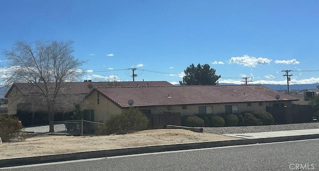 ranch-style home featuring stucco siding, a tiled roof, and fence