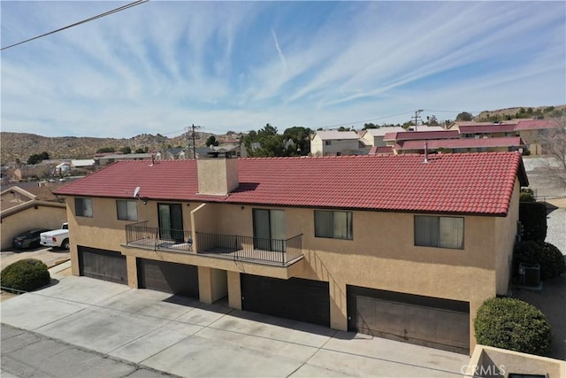 view of front of home with a tiled roof, a balcony, a chimney, and stucco siding