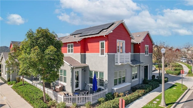 view of property exterior featuring roof with shingles, roof mounted solar panels, fence, and stucco siding