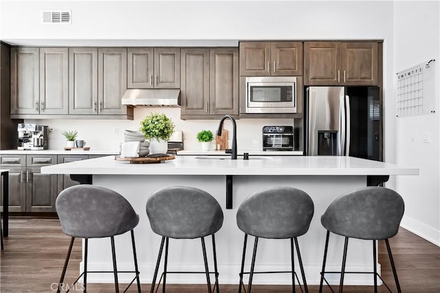 kitchen with under cabinet range hood, stainless steel appliances, dark wood-type flooring, visible vents, and light countertops