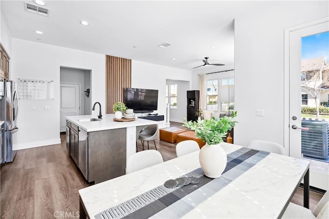 kitchen with a center island with sink, stainless steel appliances, visible vents, a sink, and wood finished floors