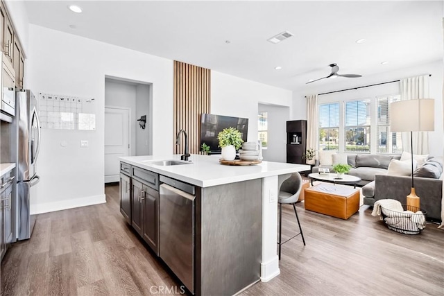 kitchen with appliances with stainless steel finishes, open floor plan, a kitchen island with sink, light countertops, and a sink