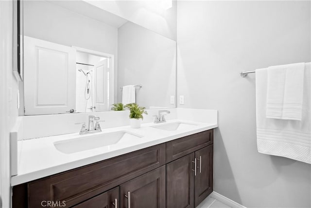 bathroom with a shower, a sink, baseboards, and double vanity