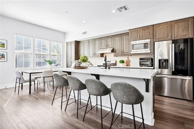 kitchen featuring stainless steel appliances, visible vents, light countertops, and under cabinet range hood