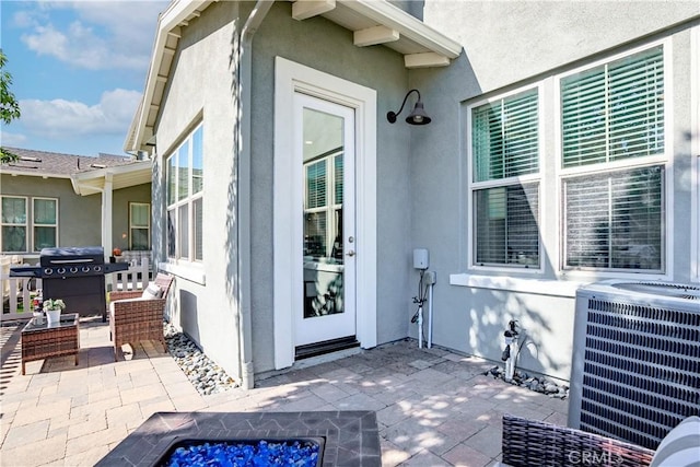 view of exterior entry with a patio area, central AC unit, and stucco siding