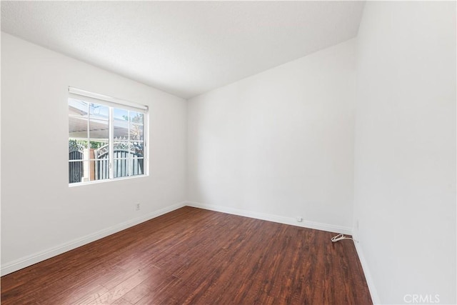 spare room featuring dark wood-style flooring and baseboards