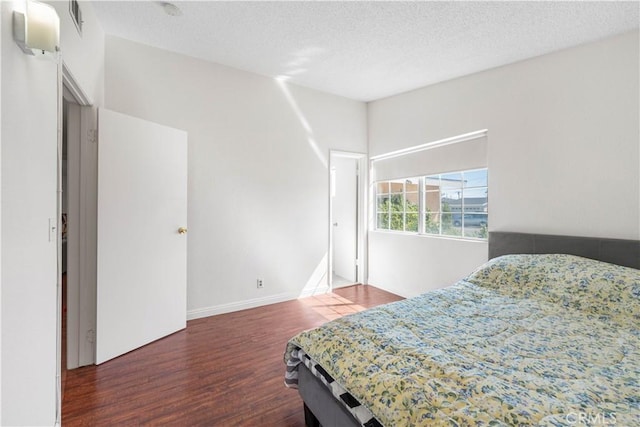 bedroom with a textured ceiling, wood finished floors, visible vents, and baseboards