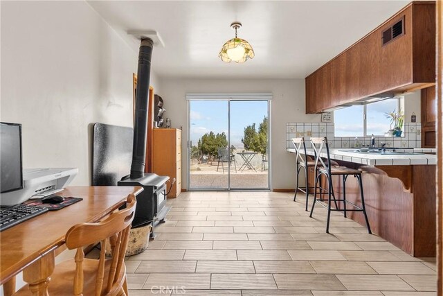 kitchen with visible vents, tasteful backsplash, tile countertops, brown cabinetry, and a wood stove