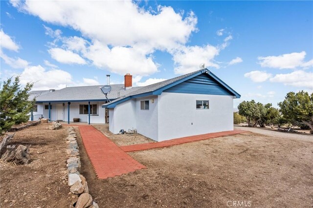 rear view of property featuring a porch, stucco siding, and a chimney