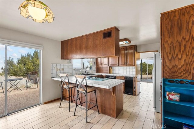 kitchen with tasteful backsplash, a healthy amount of sunlight, tile countertops, a breakfast bar area, and a peninsula