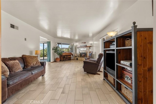 living area featuring a tiled fireplace, visible vents, and light wood-type flooring