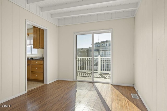 empty room with light wood-style floors, visible vents, beamed ceiling, and baseboards