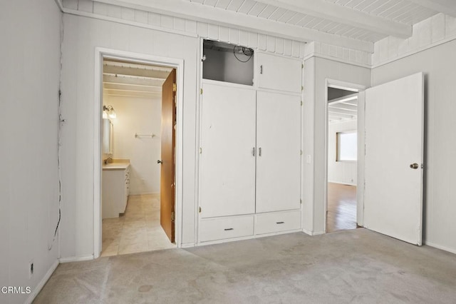 unfurnished bedroom with light carpet, beamed ceiling, and a closet