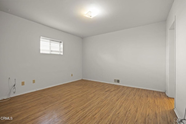 empty room with baseboards, visible vents, and wood finished floors