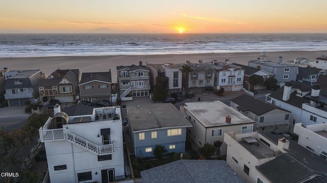 aerial view at dusk featuring a residential view, a water view, and a beach view