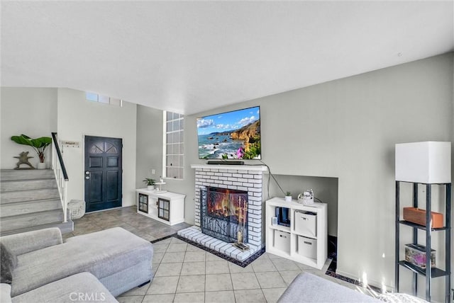 living room with a brick fireplace, visible vents, light tile patterned floors, and stairway