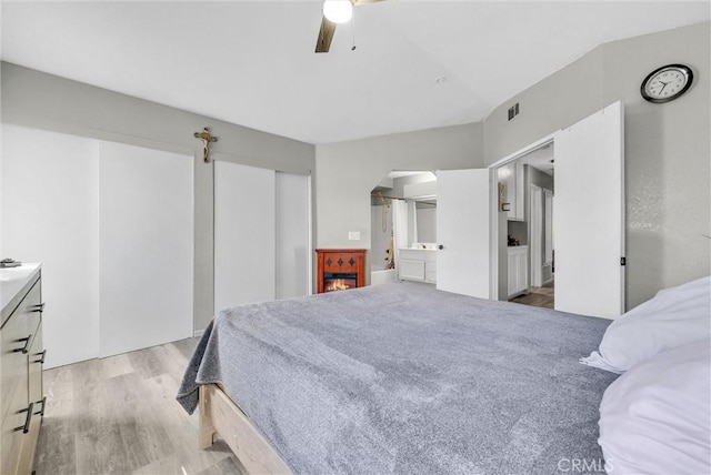 bedroom featuring arched walkways, ceiling fan, wood finished floors, visible vents, and ensuite bath