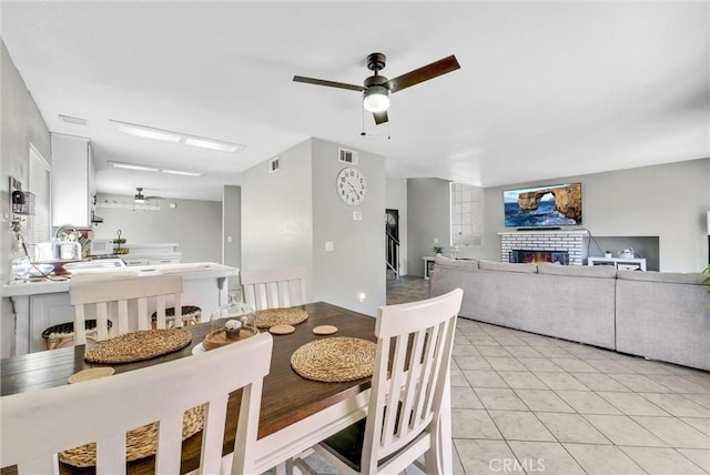 dining room featuring a warm lit fireplace, visible vents, ceiling fan, and light tile patterned floors